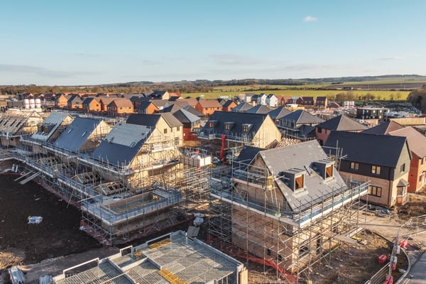 Aerial view of a housing development under construction, with multiple homes in various stages of building and scaffolding visible.
