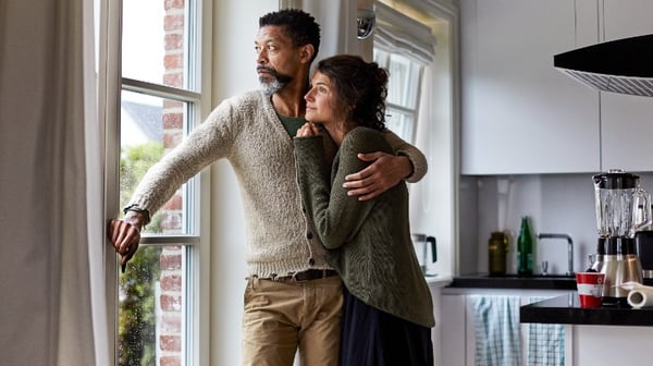 Couple standing at window looking somber