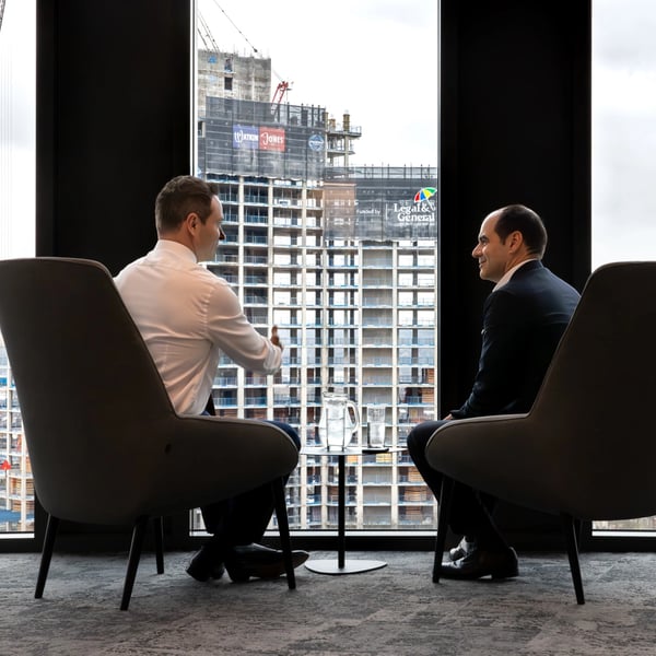 António Simões, CEO of Legal & General, seated by a window with a colleague, with construction workers visible outside.
